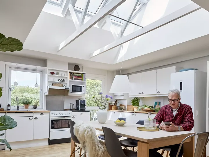 Älterer Herr sitzt in altersgerechter Küche mit großen Firstdachfenstern | VELUX Magazin
