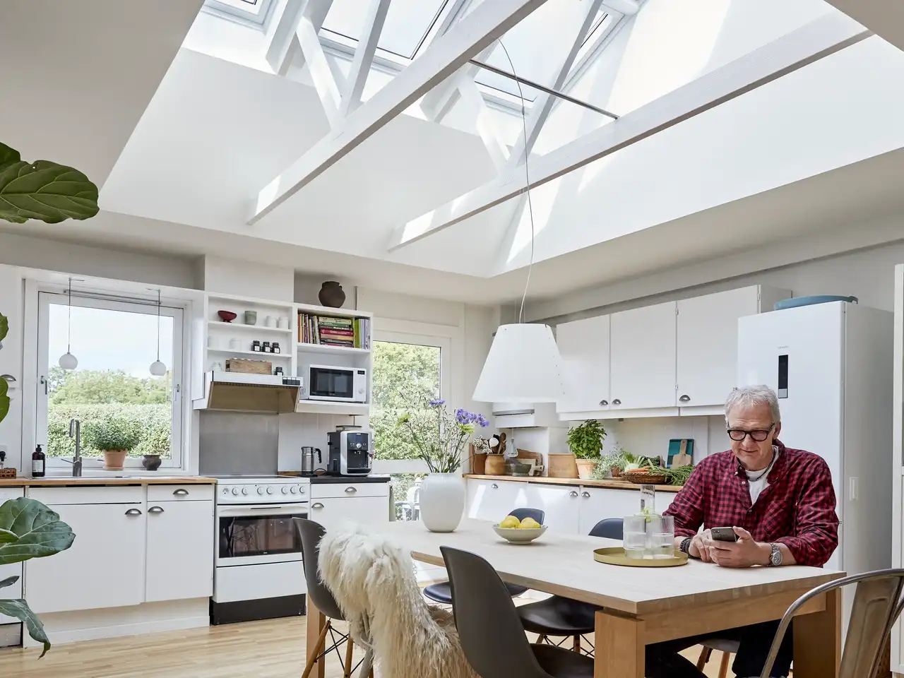 Un homme est assis dans une cuisine adaptée aux personnes âgées et équipée d’une large verrière de faîtage | Magazine VELUX