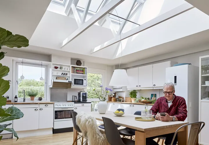 Moderne Küche mit natürlichem Licht von VELUX Dachflächenfenstern, weißen Schränken und einem Essbereich.