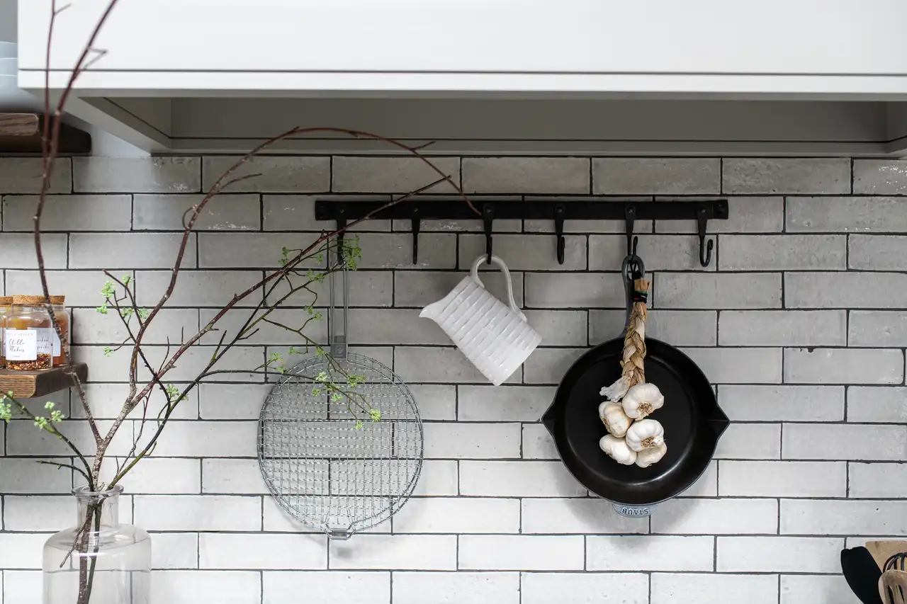 Kitchen wall with rustic decor, garlic braid, ceramic jug, and subway tiles.