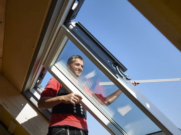 Dachdecker montiert ein Dachfenster bei Sonnenschein und blauem Himmel | VELUX Magazin