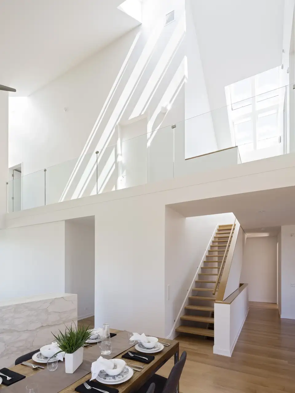 Pièce de vie avec mezzanine à garde-corps vitré et fenêtres de toit sous une charpente inclinée.