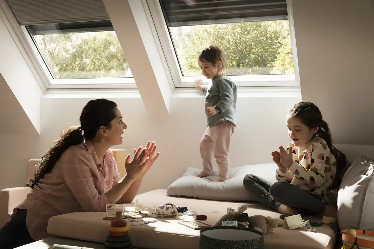 Frau und zwei Kinder spielen auf Sofa unter Dachfenstern | VELUX Magazin
