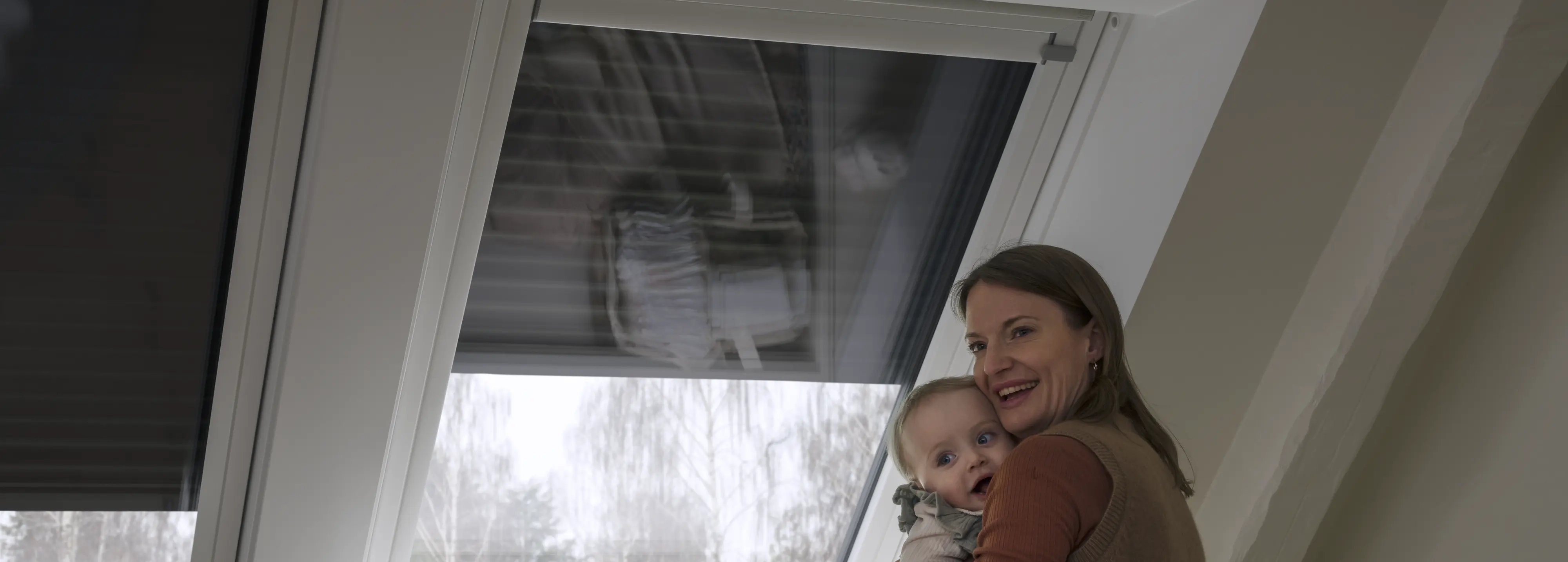 Attic kid's room with sloped ceiling and large VELUX roof windows, natural light entering. Mother and baby.