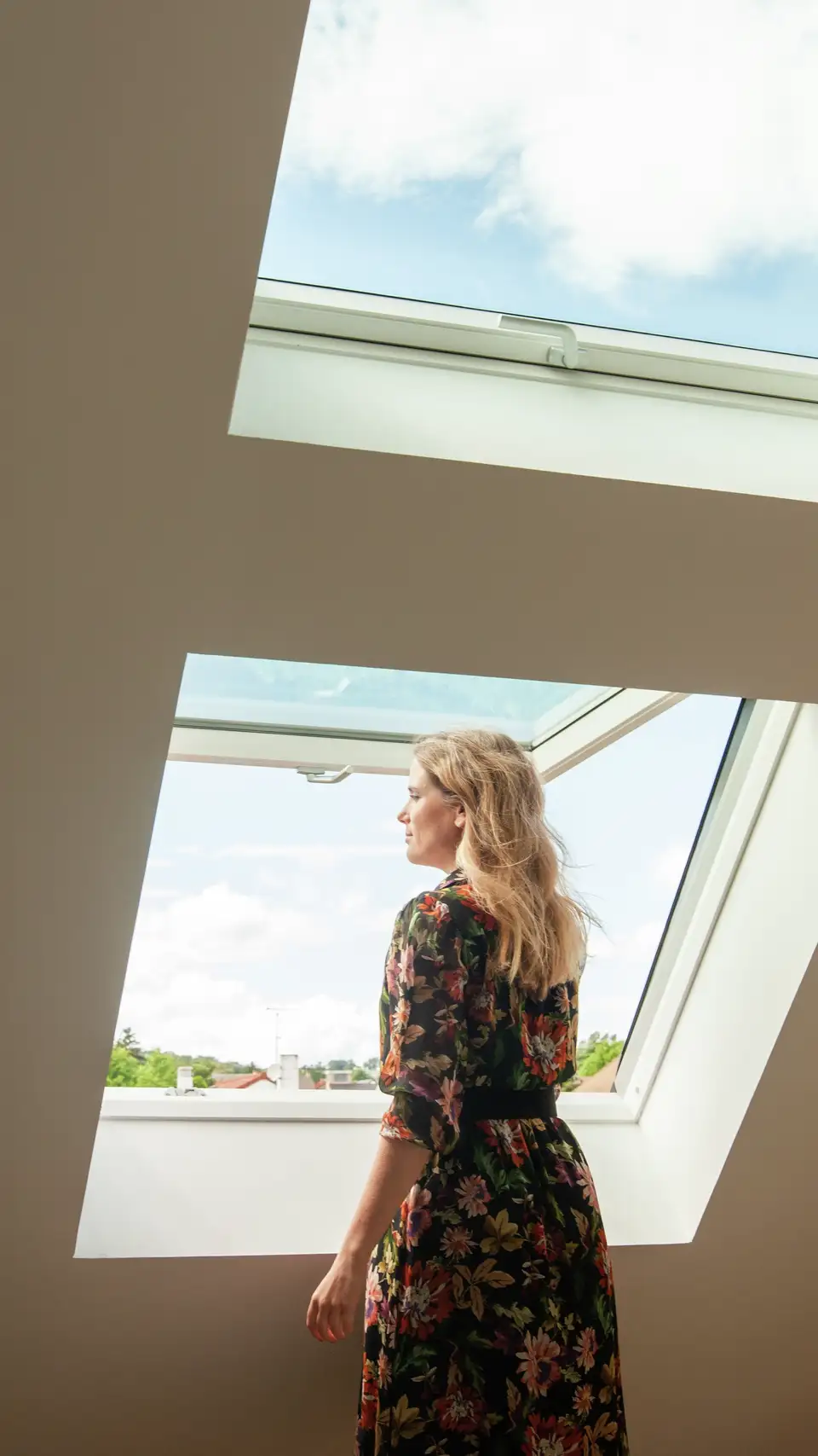 Femme regardant par une fenêtre de toit VELUX dans une pièce sous les toits