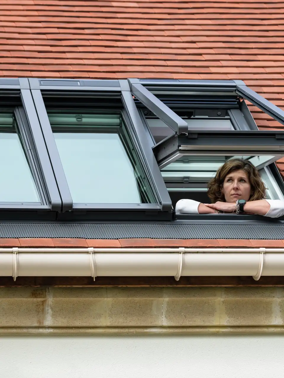 Detail van een hellend dak met een VELUX 3in1 dakvenster, waarvan er een open staat en waarop een persoon leunt