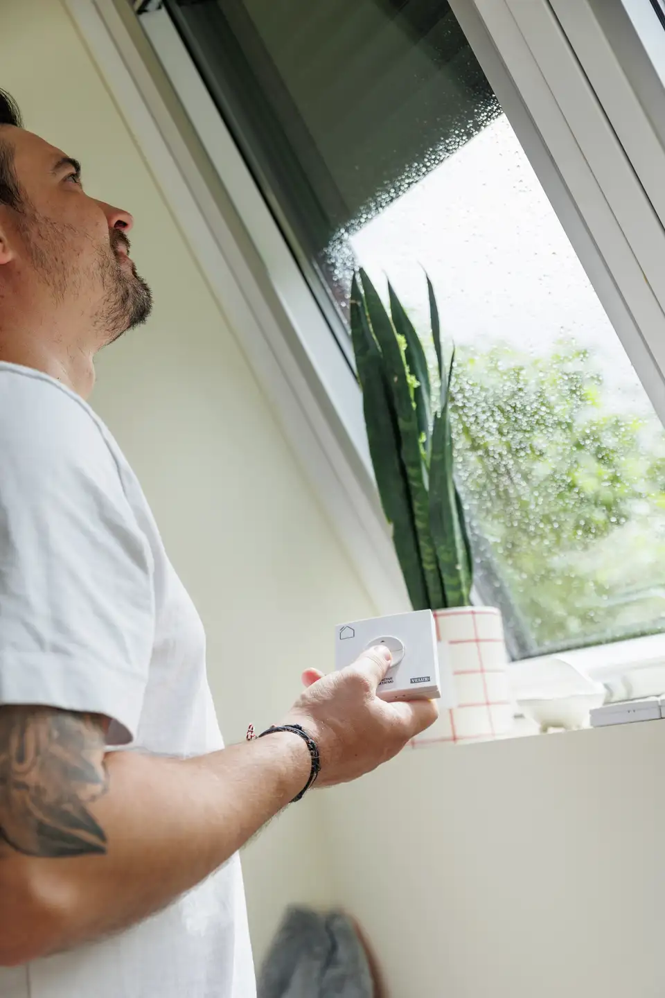Osoba koja koristi daljinski upravljač za VELUX krovni prozor, pogled na kišu vani.
