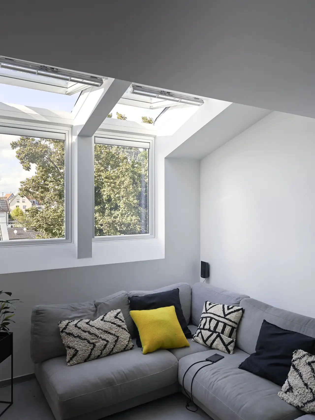 Zona living con divano angolare sotto due finestre verticali e due finestre per tetti affiancate.