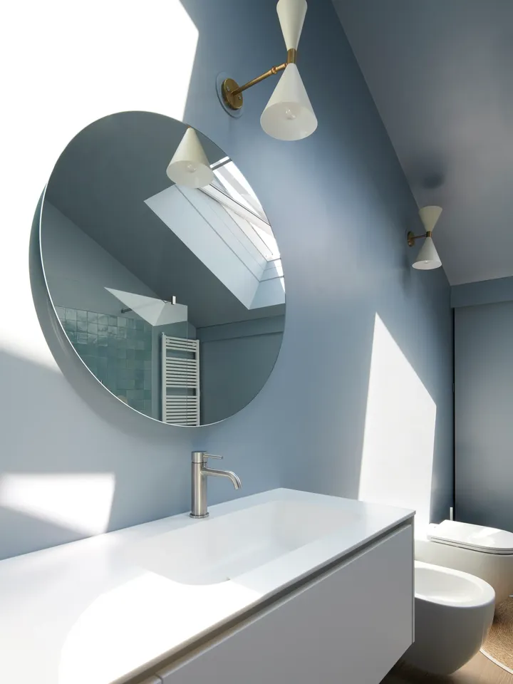 Modernes Badezimmer mit weißem Waschbecken, rundem Spiegel und VELUX Dachflächenfenster, das sich im Spiegel spiegelt.