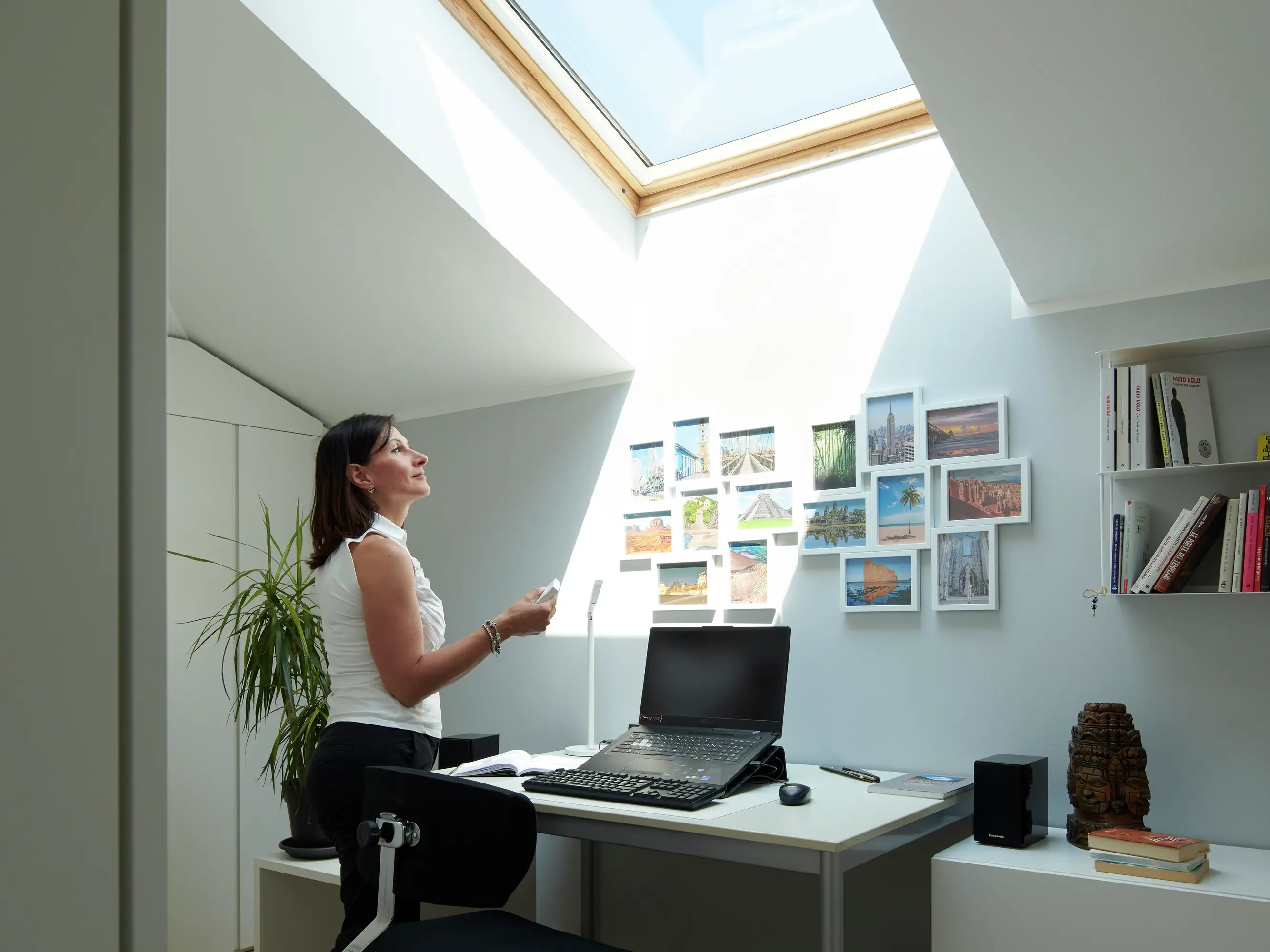 Une femme dans son studio ouvre une fenêtre de toit à l'aide d'une télécommande.