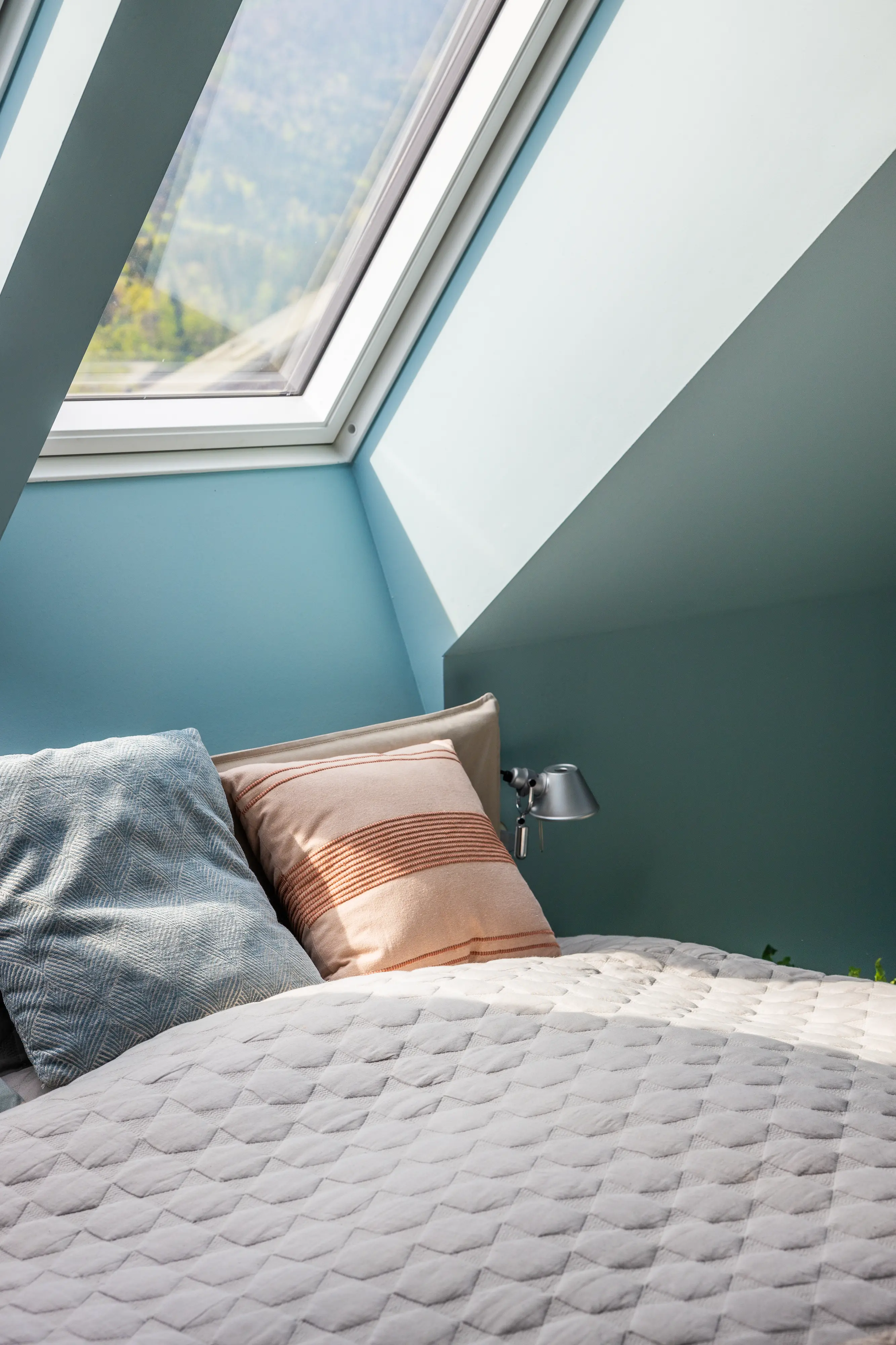 Chambre sous combles avec murs verticaux et plafond incliné peints en bleu clair. 