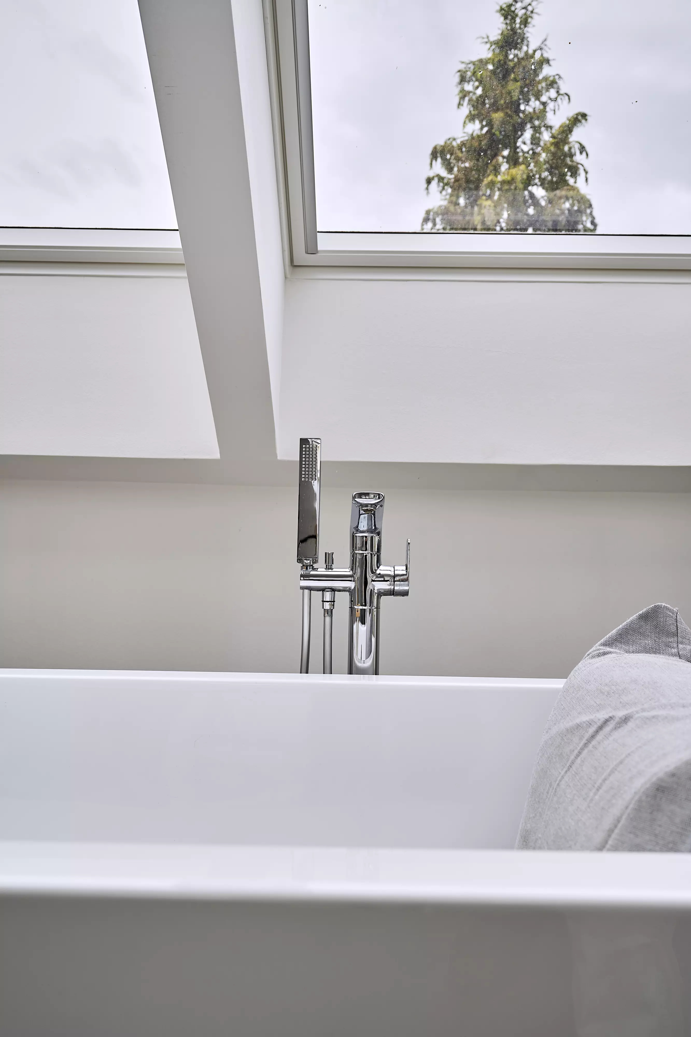 Weiße Badewanne mit Chromarmatur unter einem VELUX Dachflächenfenster mit Blick auf einen Baum.
