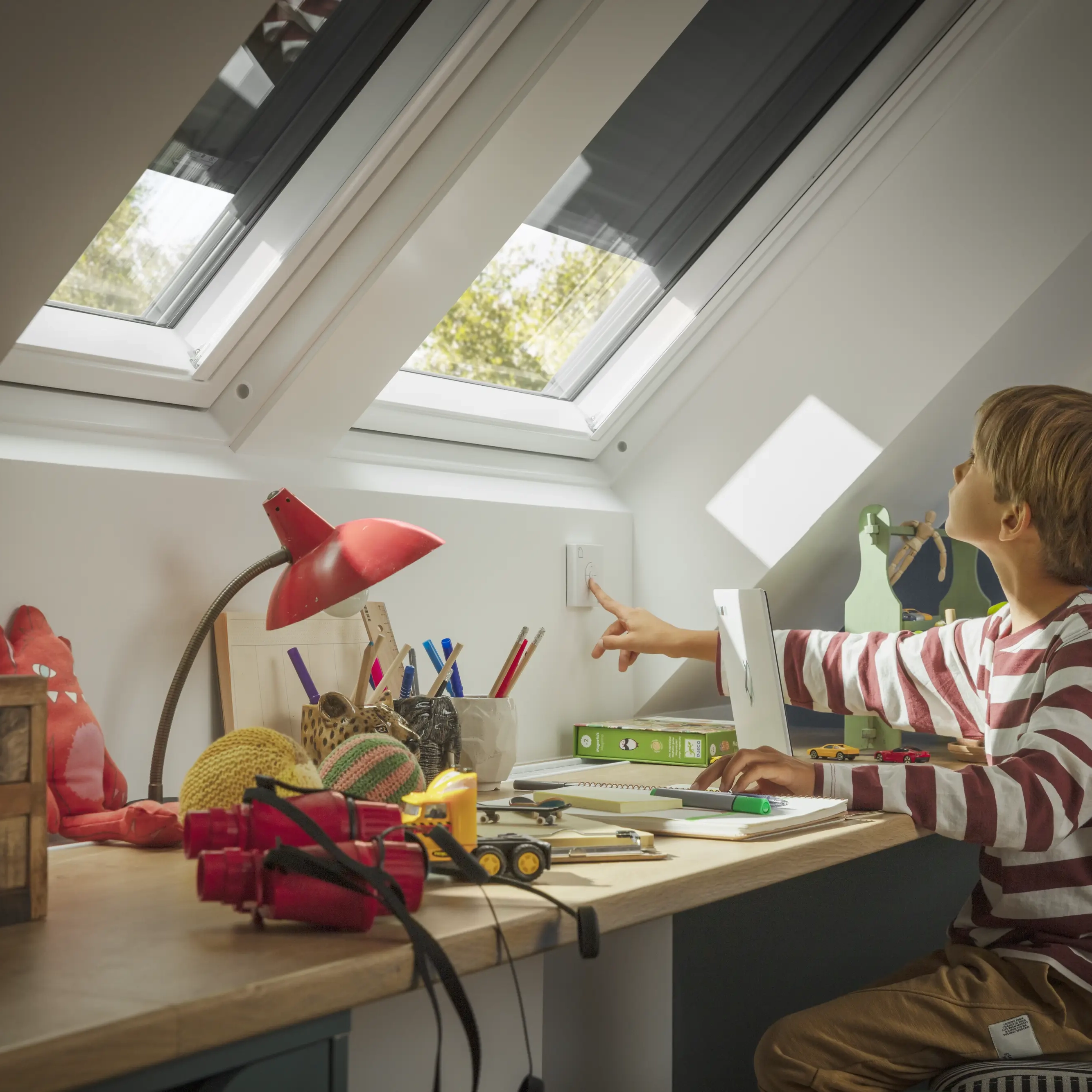 Attic study space with sloped ceiling and VELUX roof windows, child at desk.