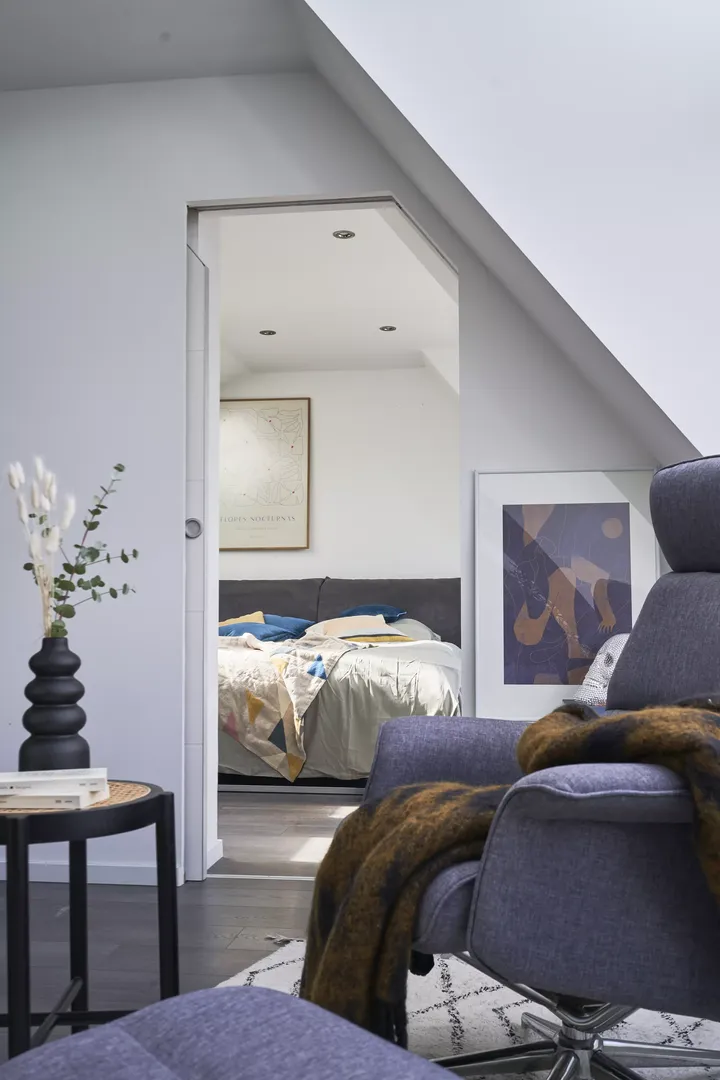 Aussicht in ein Dachboden-Schlafzimmer mit einem VELUX Dachflächenfenster und bunter Bettwäsche, umrahmt von einem Sessel.