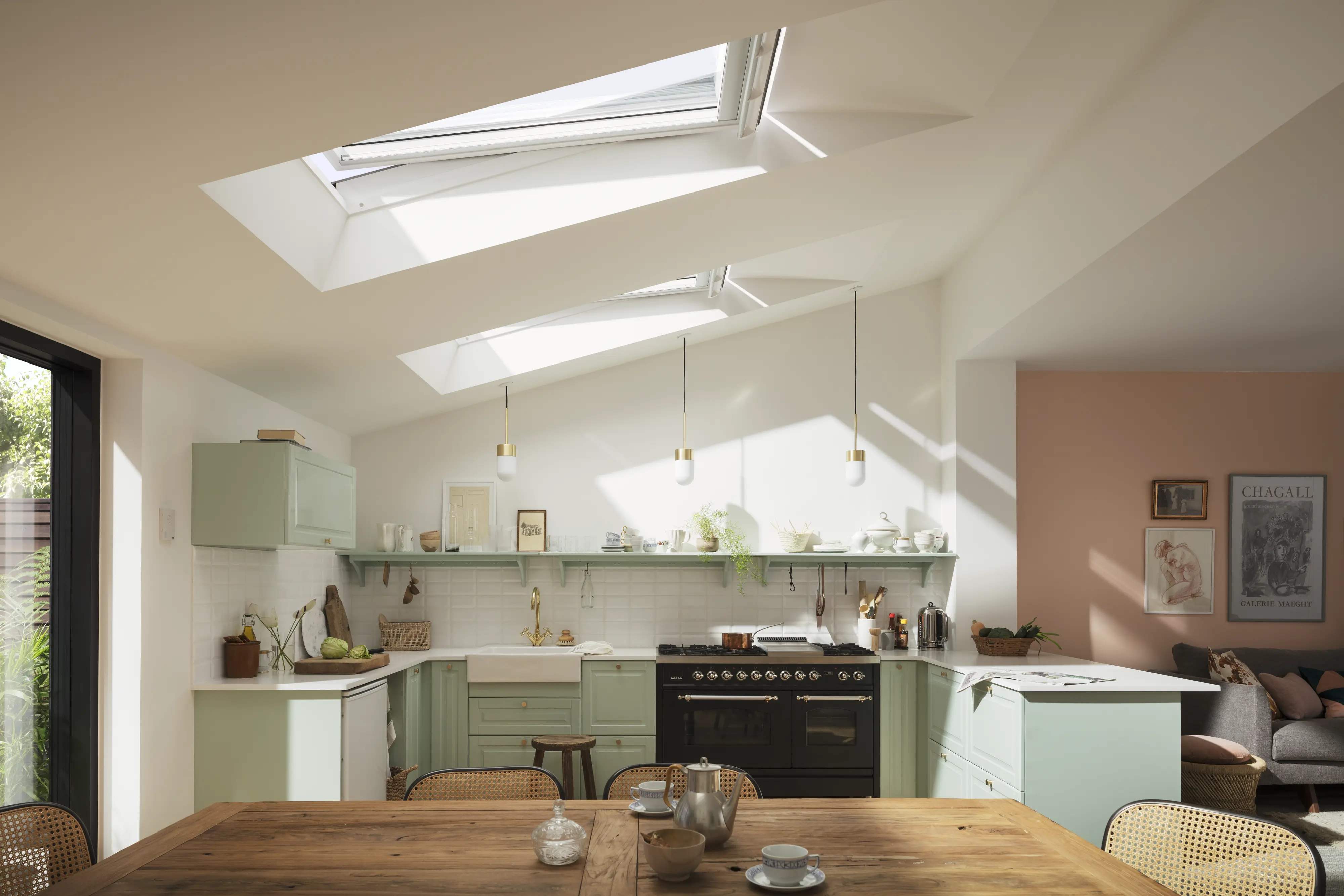 Cucina verde chiaro con tavolo in legno illuminata da due finestre per tetti VELUX