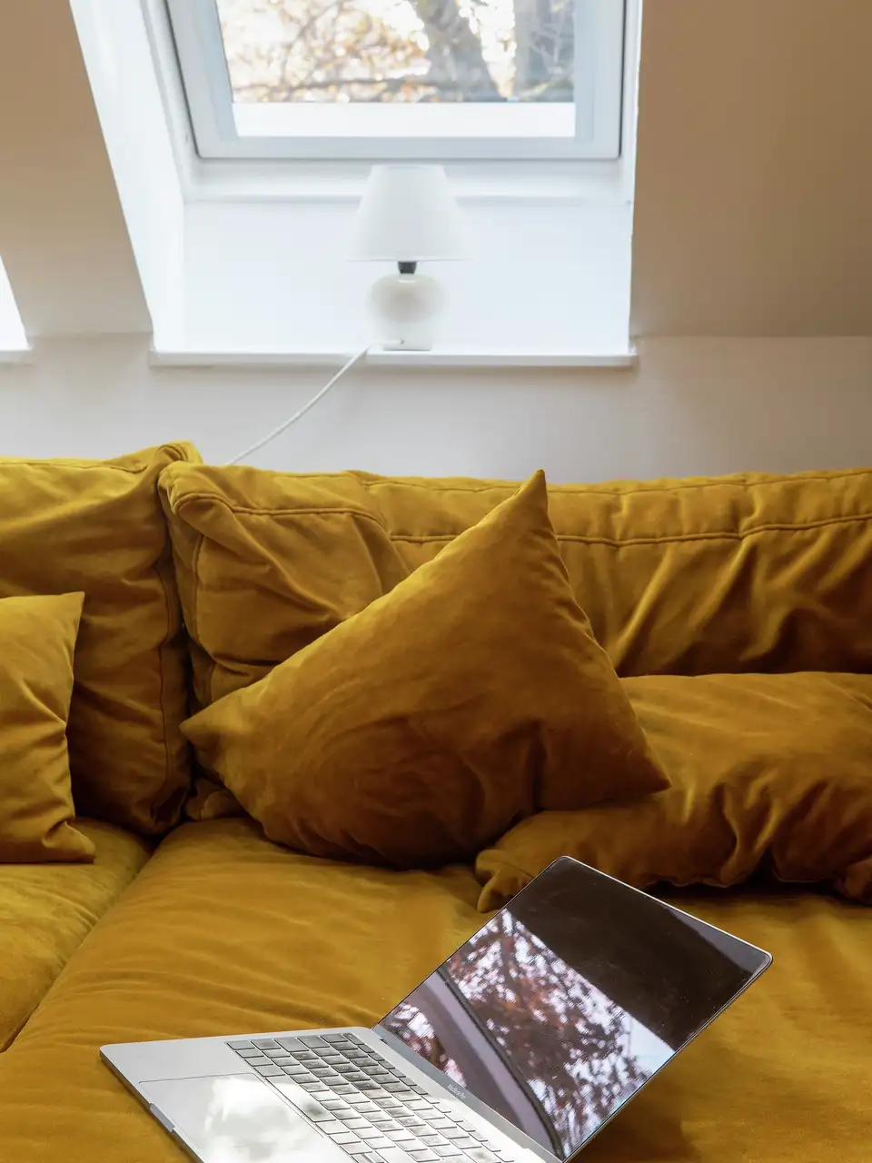 Mansarda con divano color senape sotto finestra per tetti VELUX.