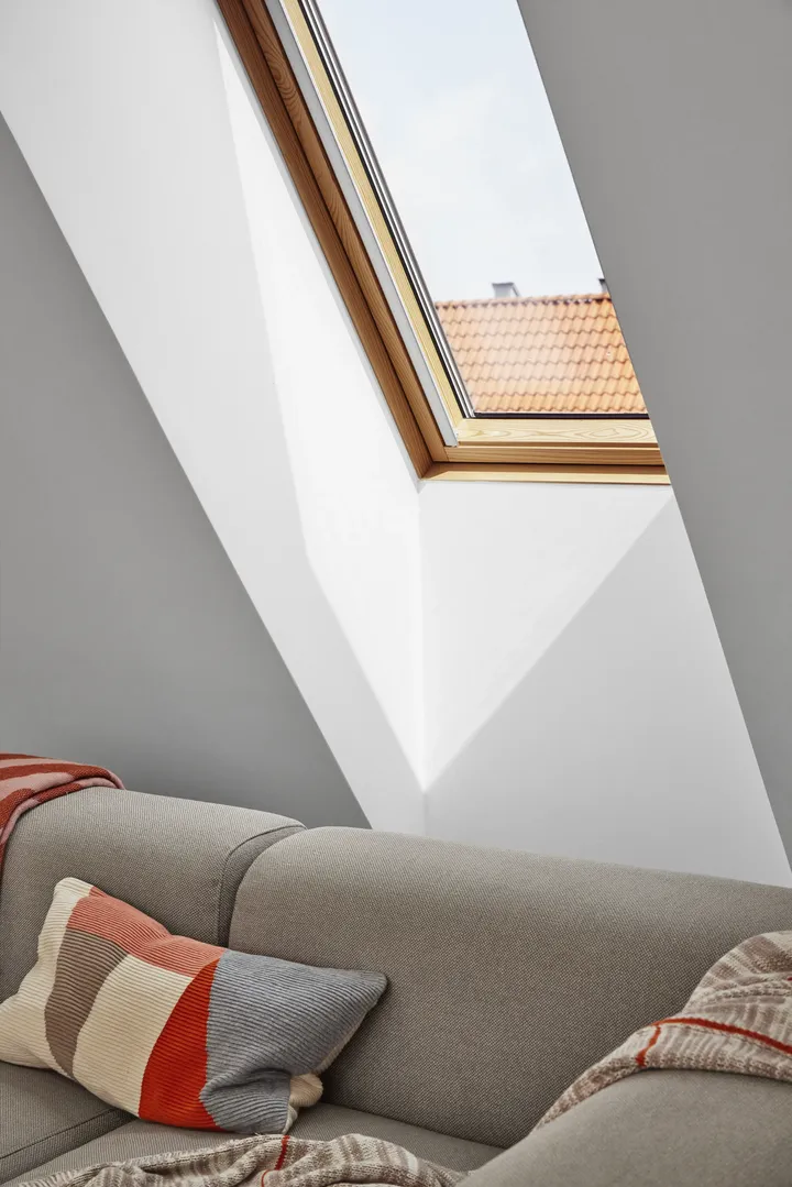 Таванско помещение със скосен таван и покривен прозорец VELUX, уютен диван с възглавници.