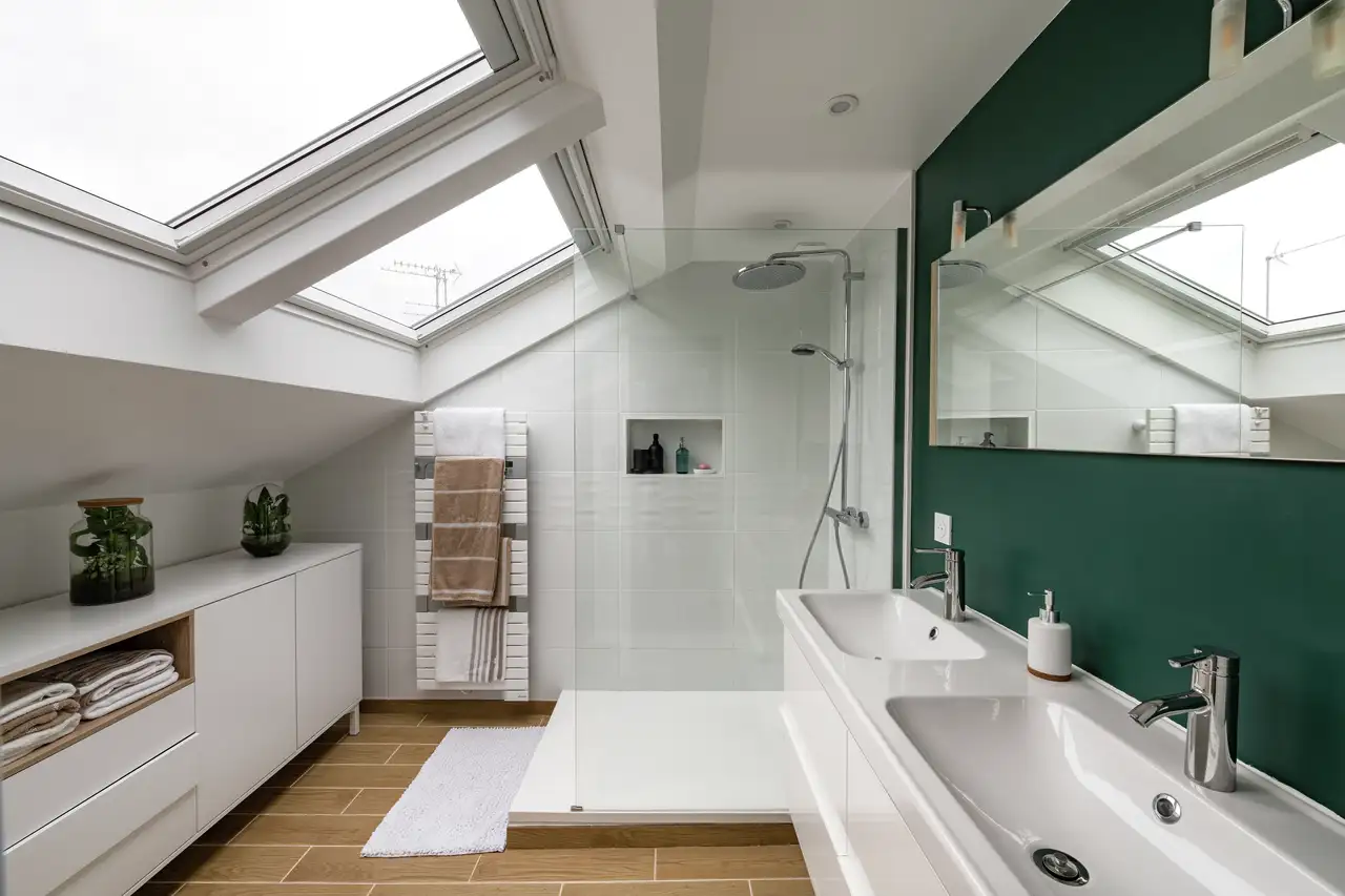 Salle de bains moderne avec mur bleu d’accent, baignoire îlot et fenêtre de toit apportant une lumière naturelle abondante.