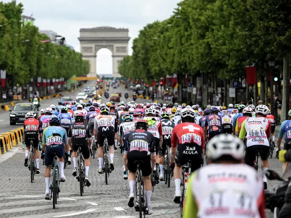 Kolesarji vozijo po aveniji Champs-Élysées s Slavolokom zmage v ozadju med dirko Tour de France.