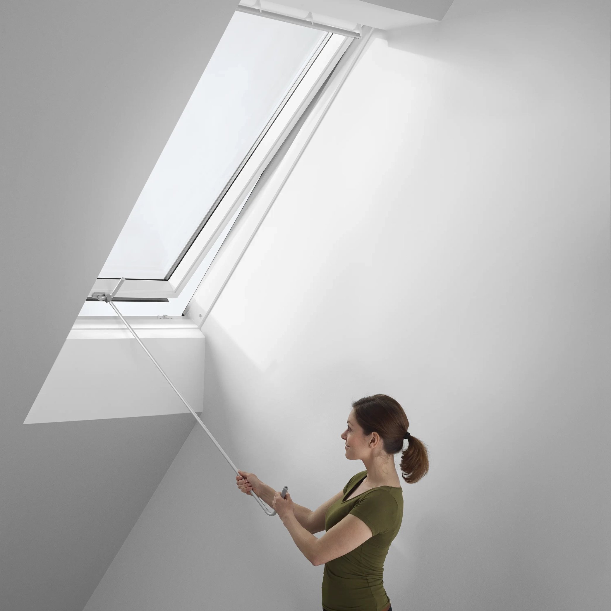 Attic room with sloped ceiling and VELUX roof window being opened with a pole.
