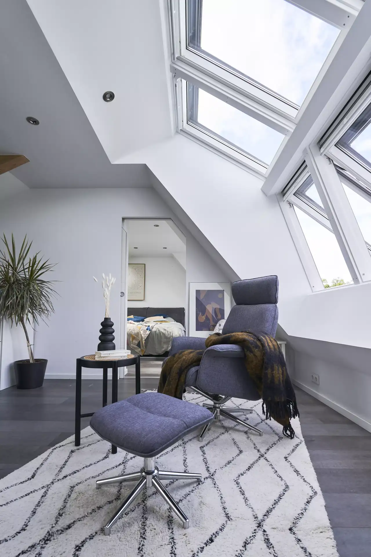 Zeitgemäßes Wohnzimmer im Dachboden mit VELUX Dachflächenfenstern und gemütlichem blauen Sessel.