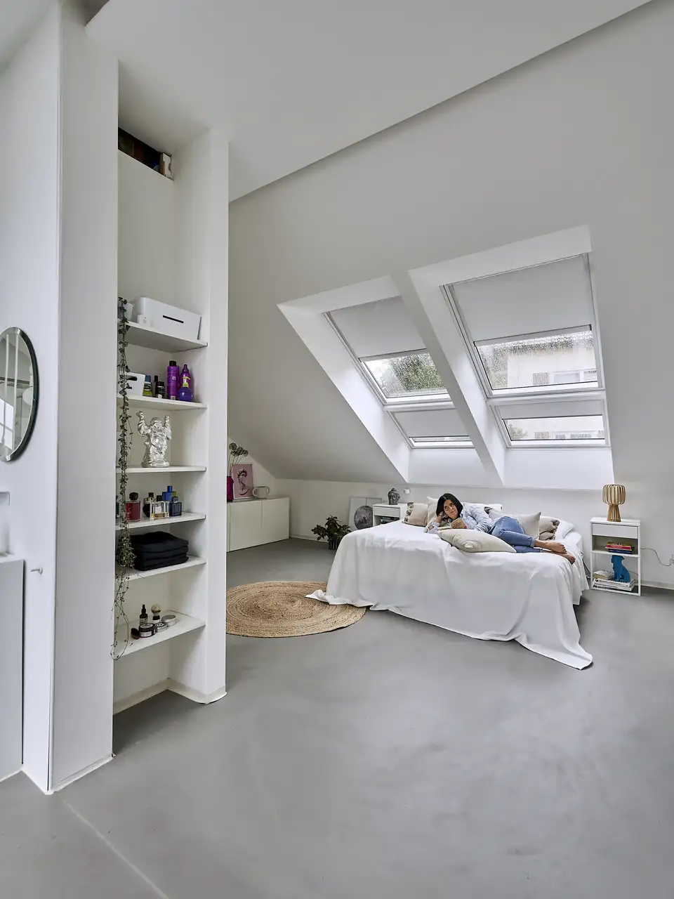 camera in mansarda con letto sotto a due grandi finestre per tetti, copriletto bianco e una donna stesa sul letto