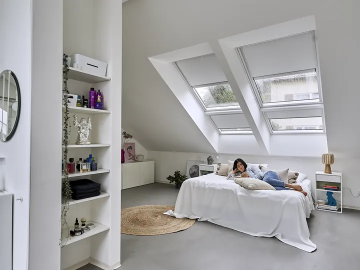 Frau im Bett unter zwei Dachfenstern im Schlafzimmer mit Einbau-Regallösung als Raumteiler zum Bad  | VELUX Magazin
