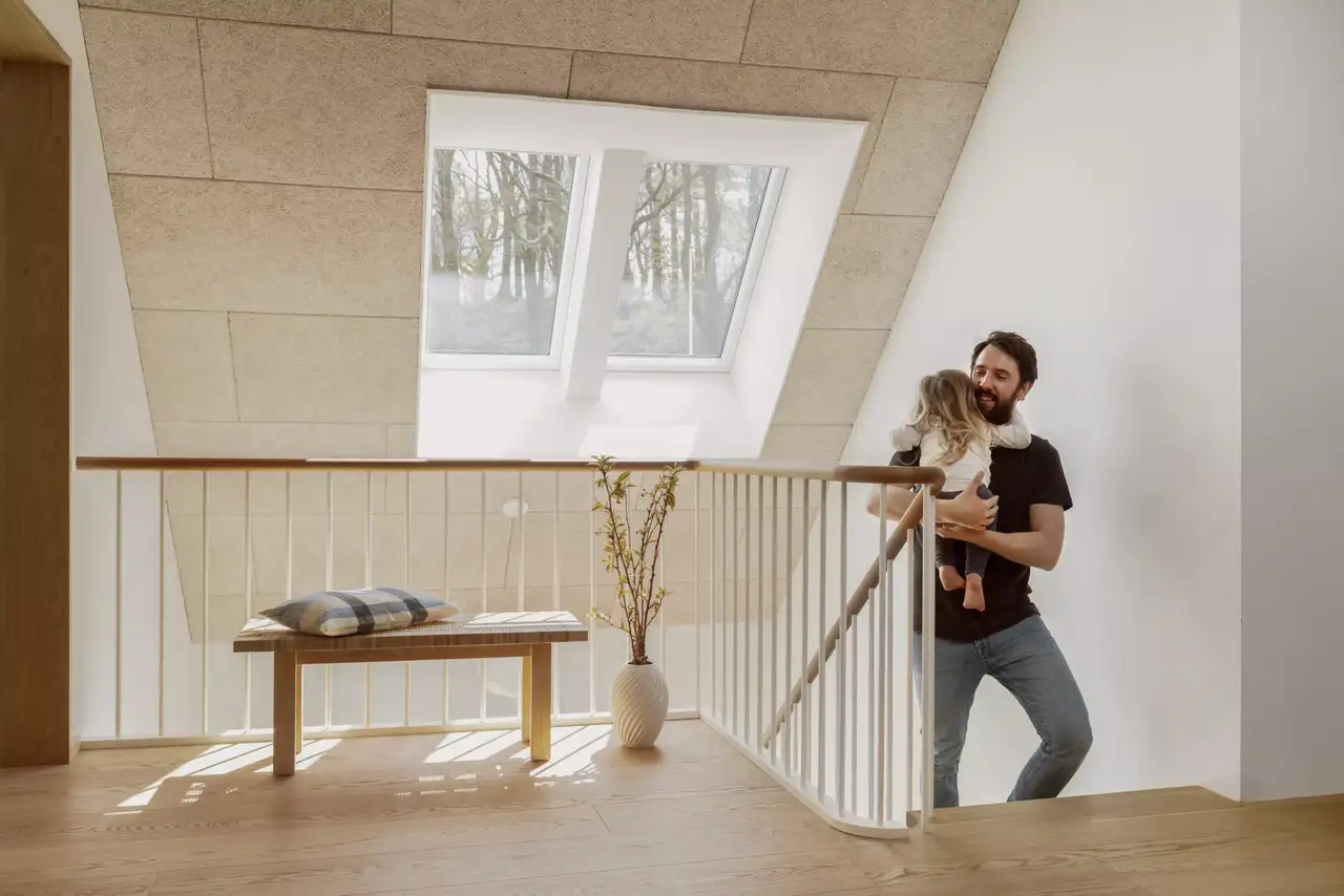 Otac drži svoju kćer u naručju i hoda uz stepenice, iza njih se vidi veliki VELUX krovni prozor