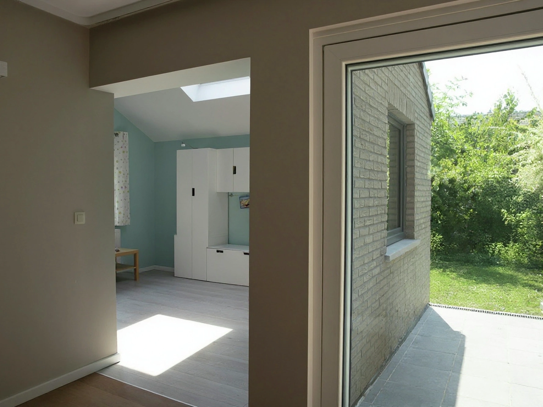 Zicht vanuit het huis op de nieuwe speelkamer, verlicht door een VELUX dakvenster, naast de schuifdeur naar de tuin