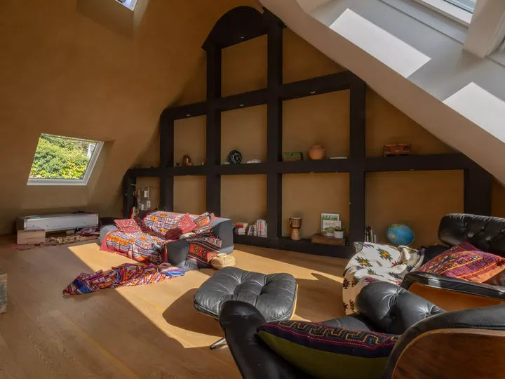 Sonnendurchfluteter Dachboden-Wohnraum mit VELUX-Fenster, dunklen Regalen und bunten Kissen.