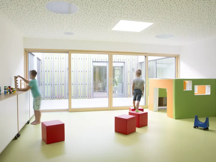 Kindertagesstättenraum mit natürlichem Licht von VELUX Dachflächenfenstern, bunten Bausteinen und spielenden Kindern.