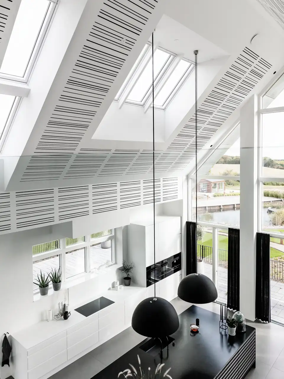 Cucina moderna in una mansarda con soffitto alto e sospensioni che partono dalle nicchie delle finestre per tetti