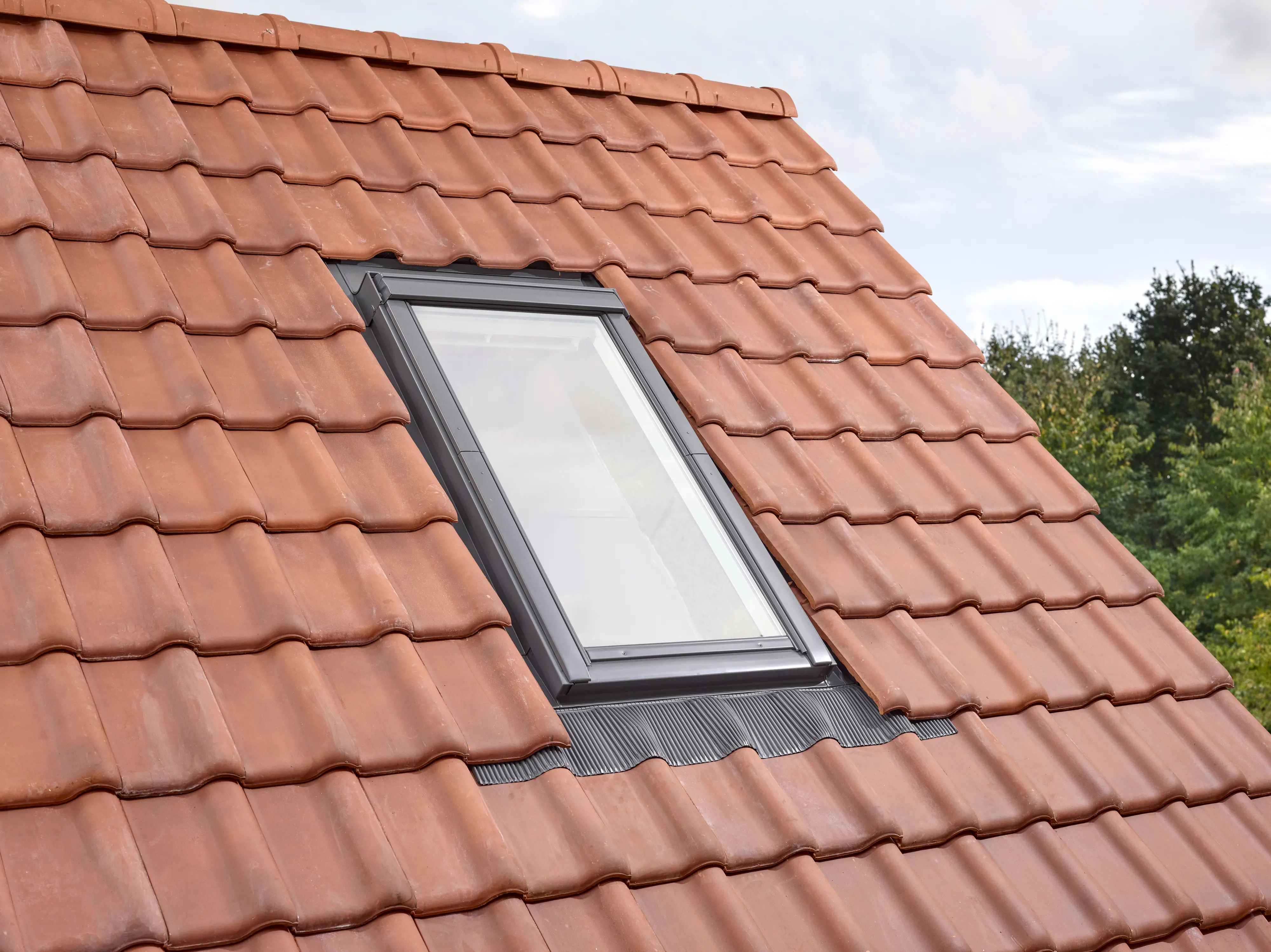 Staré strešné okno inštalované v jednej rovine so strešnými škridlami, vykazujúce známky opotrebenia na šikmej streche. | VELUX