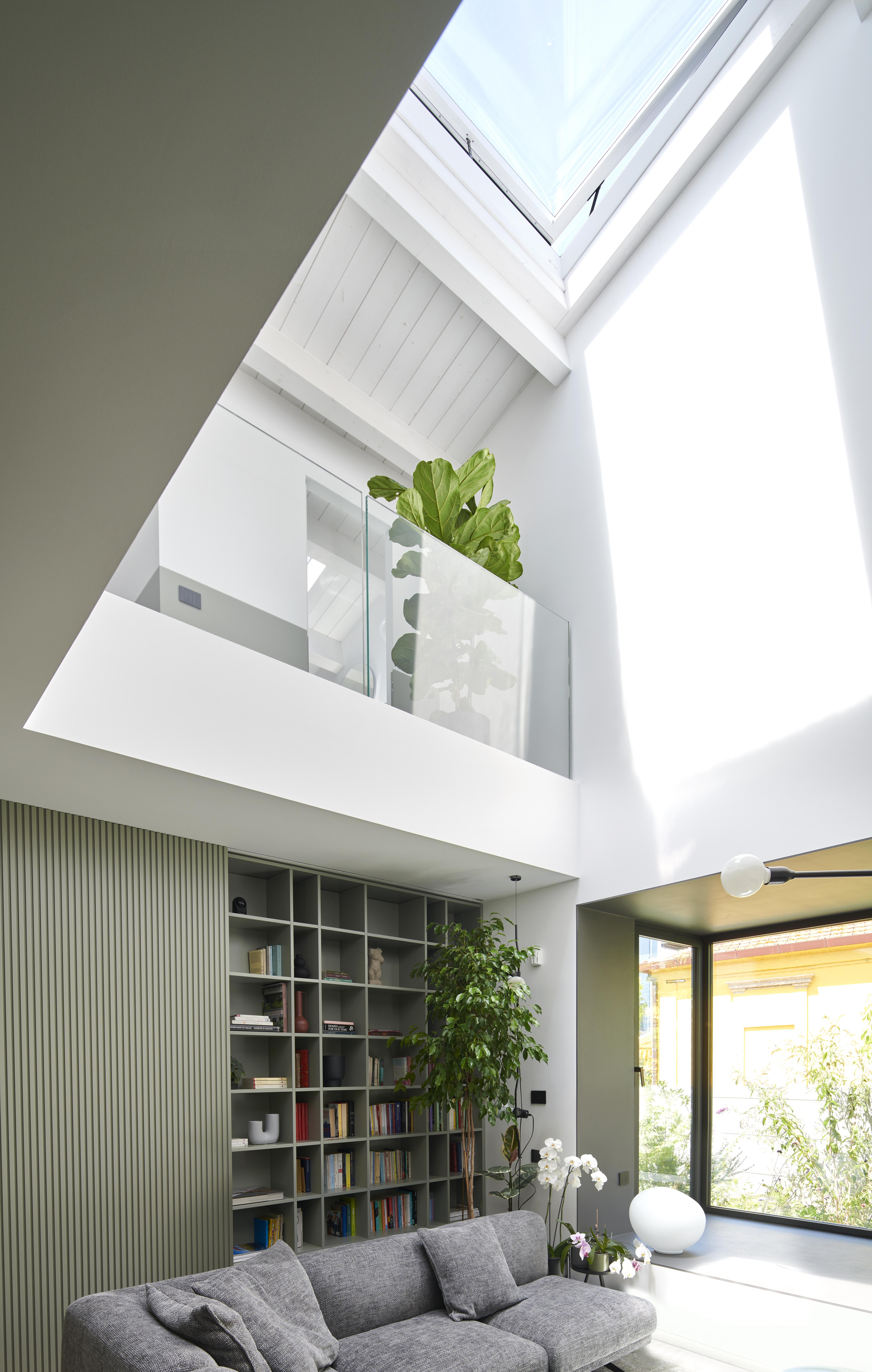 Soggiorno moderno con finestra per tetti VELUX, divano grigio, libreria e piante da interno.