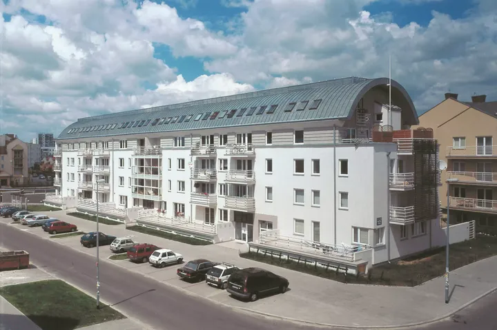 Modernes Apartmentgebäude mit geschwungenem Dach und VELUX Dachflächenfenstern unter einem blauen Himmel.
