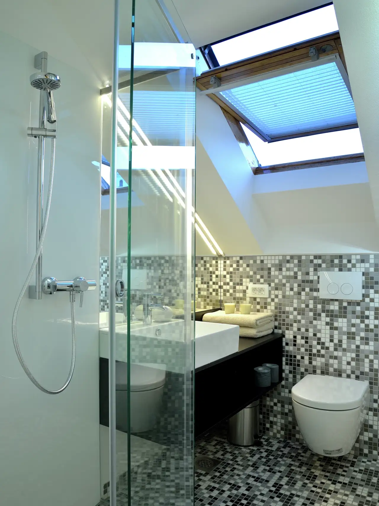 Bagno con finestra per tetti, piastrelle a mosaico e doccia in vetro. 