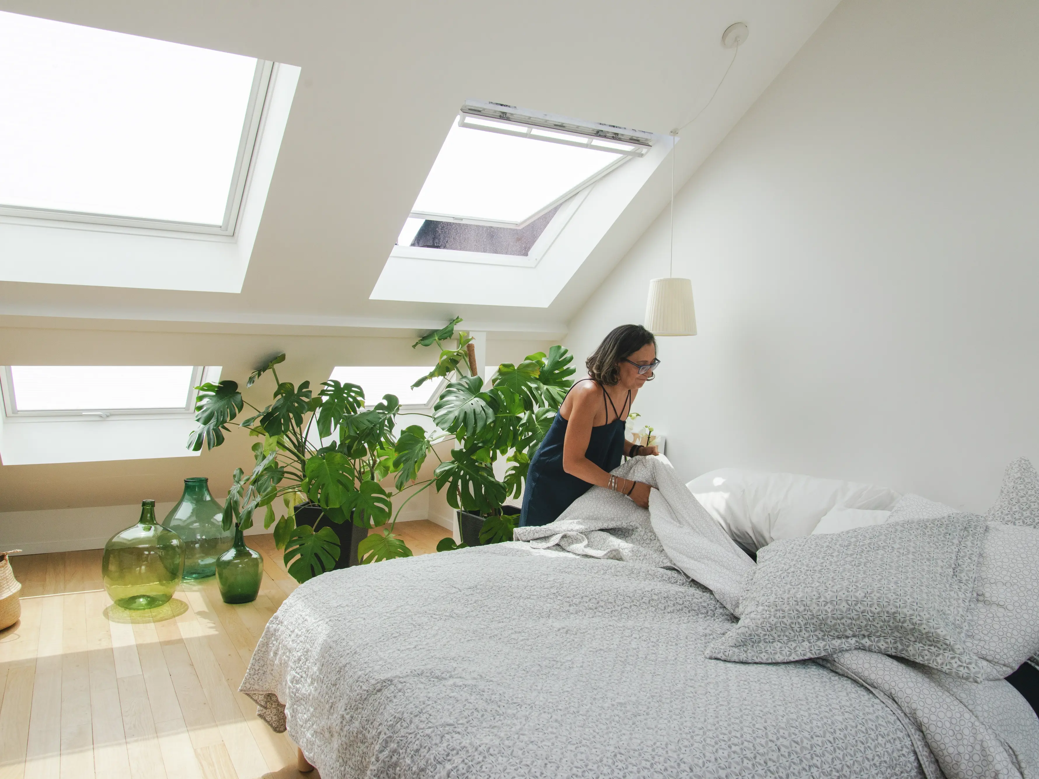 Chambre mansardée confortable avec fenêtres de toit VELUX, plantes et décoration minimaliste.