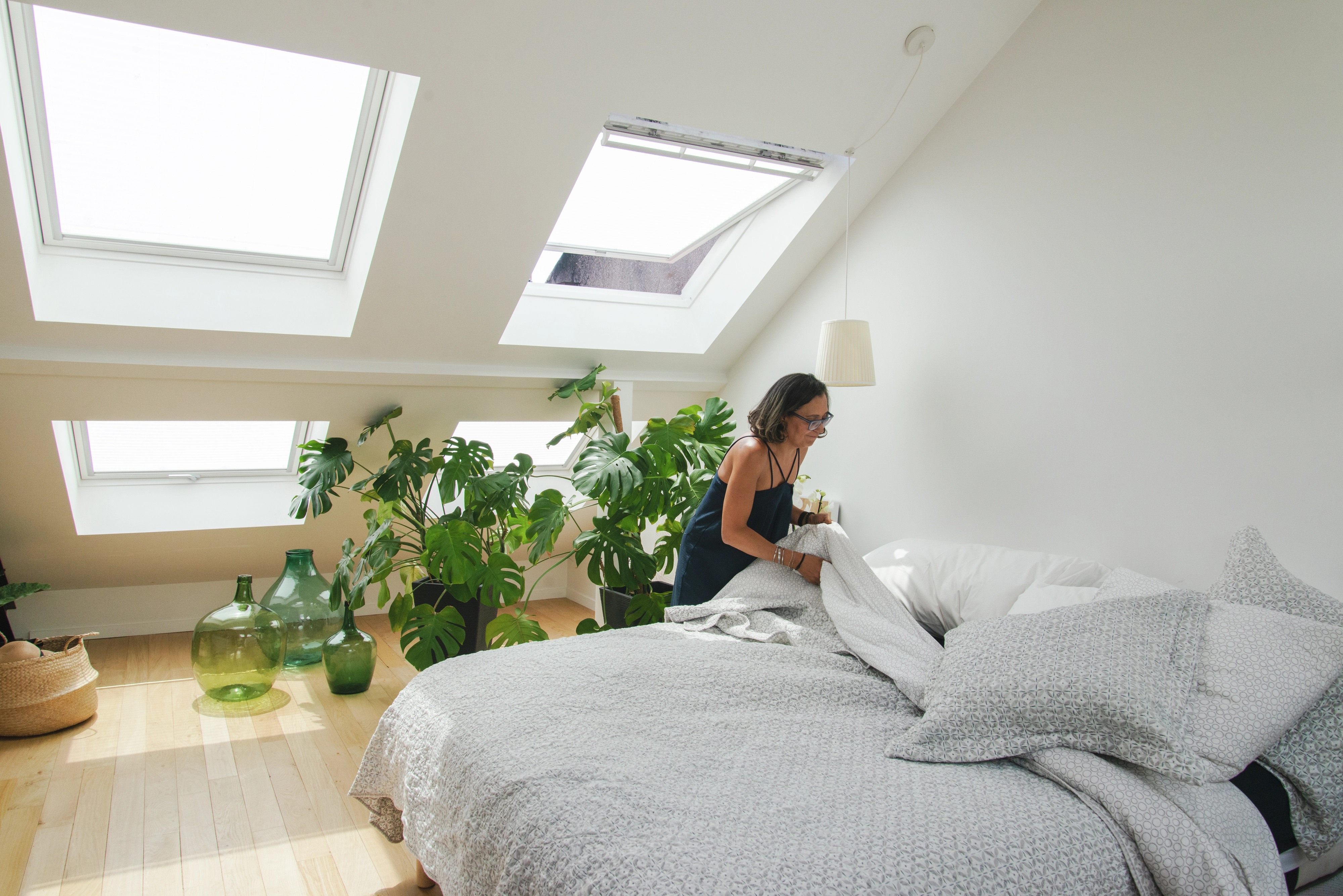 Camera da letto luminosa con finestre per tetti VELUX, piante e una coperta grigia sul letto.