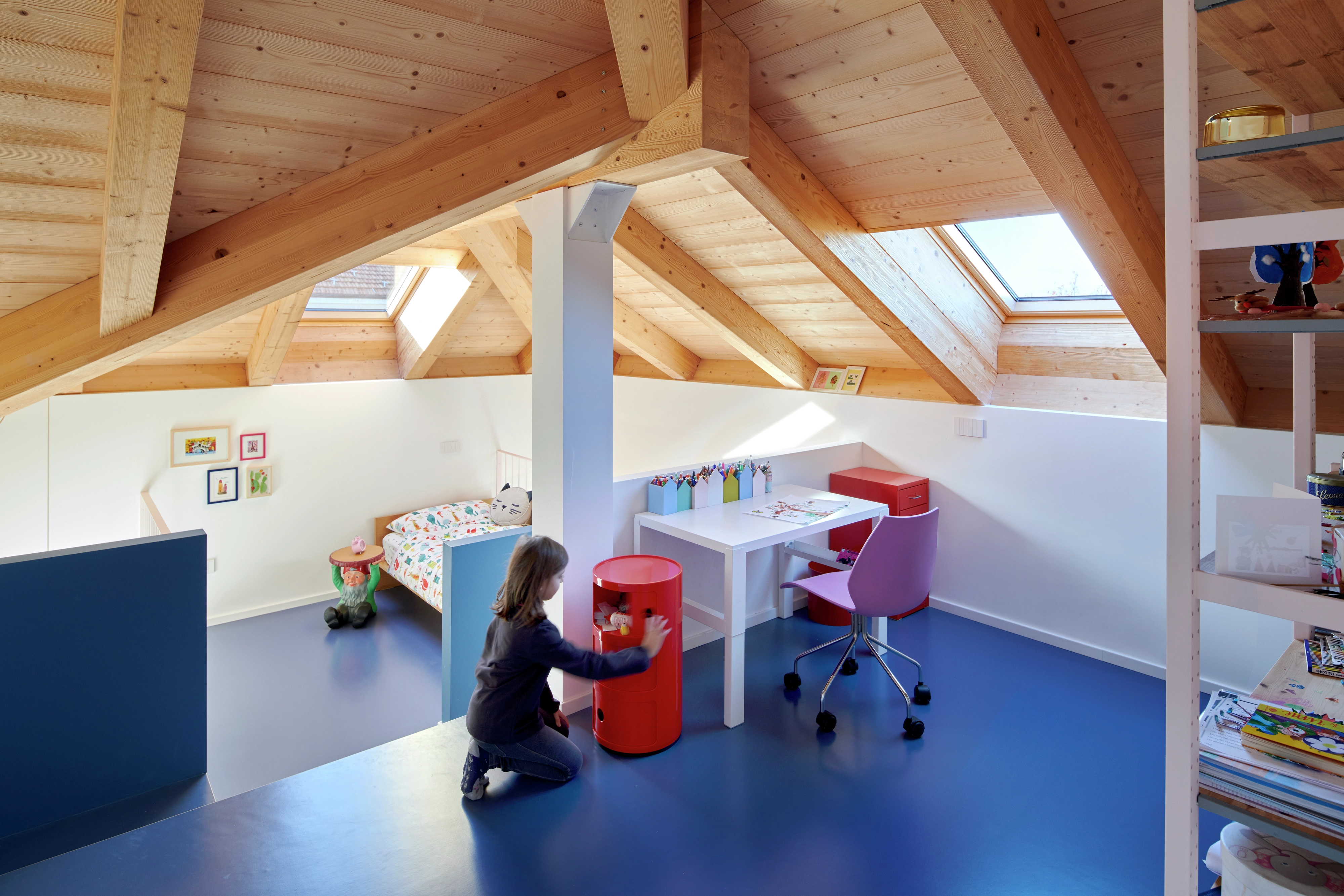 Sala giochi per bambini in mansarda con finestre per tetti VELUX, travi in legno e mobili colorati.