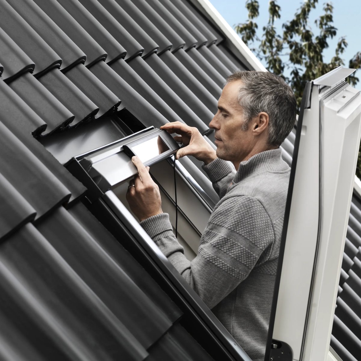 Person installing VELUX roof window on a sloped roof with dark tiles.