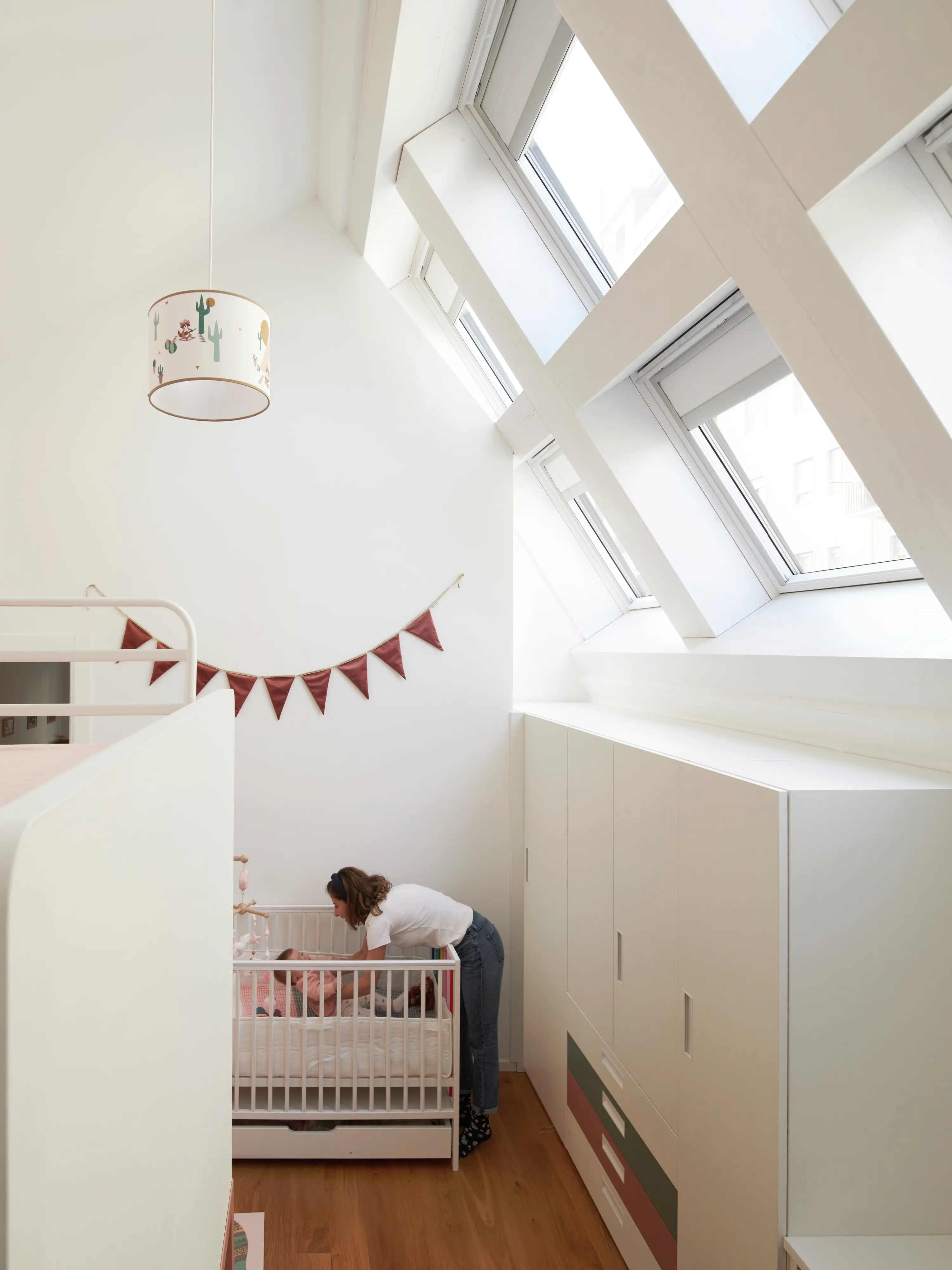 Accogliente camera per bambini in mansarda con luce naturale proveniente dalle finestre per tetti VELUX, culla e spazio di archiviazione.