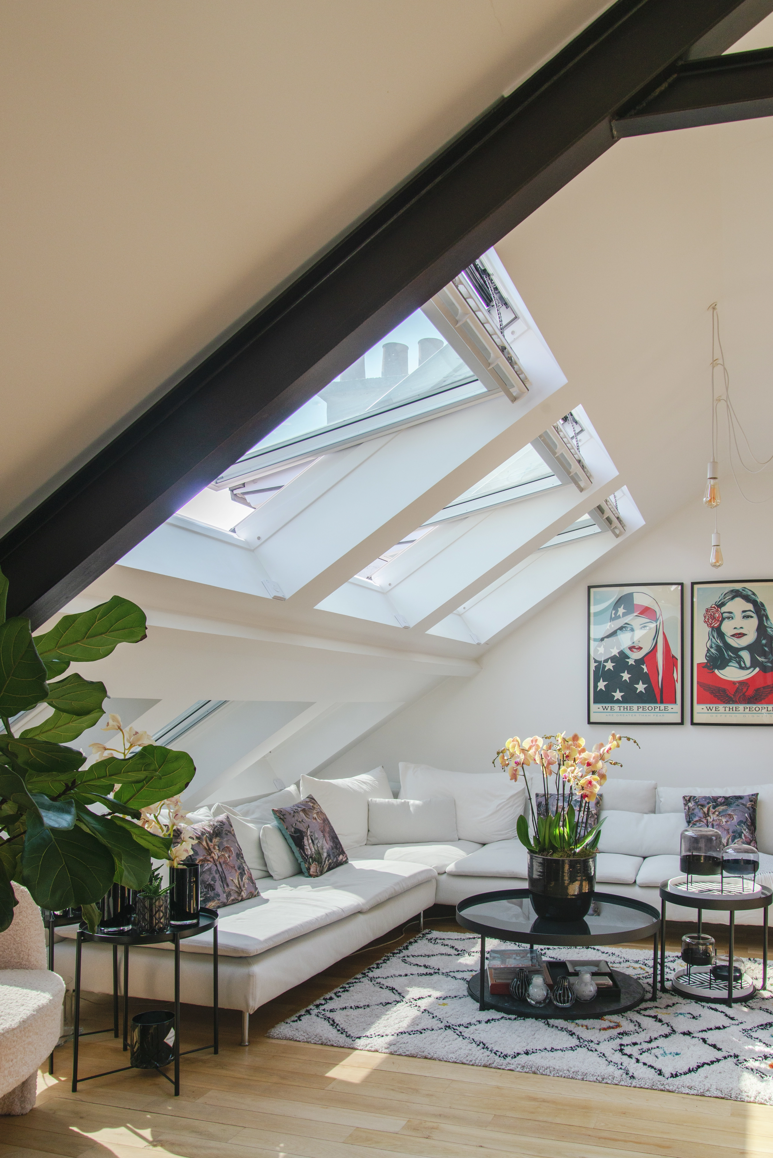 Salon moderne dans les combles avec des fenêtres de toit VELUX, un canapé d'angle et des plantes d'intérieur.