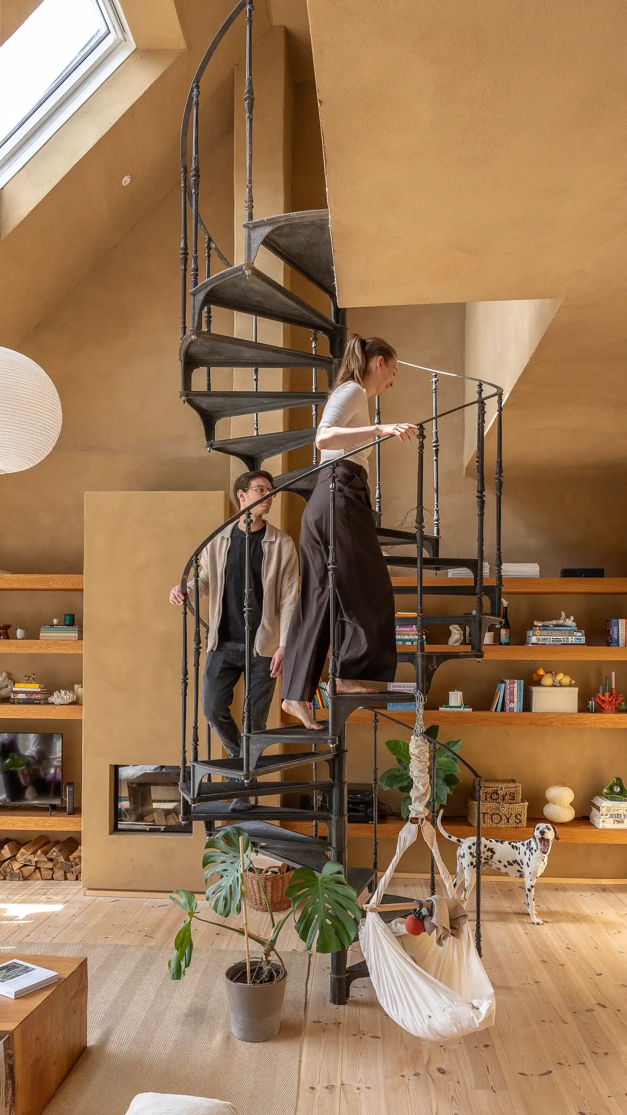 Ein Paar auf einer Wendeltreppe in einem warmen Wohnzimmer, erhellt von natürlichem Licht durch VELUX Dachfenster. | VELUX Magazin