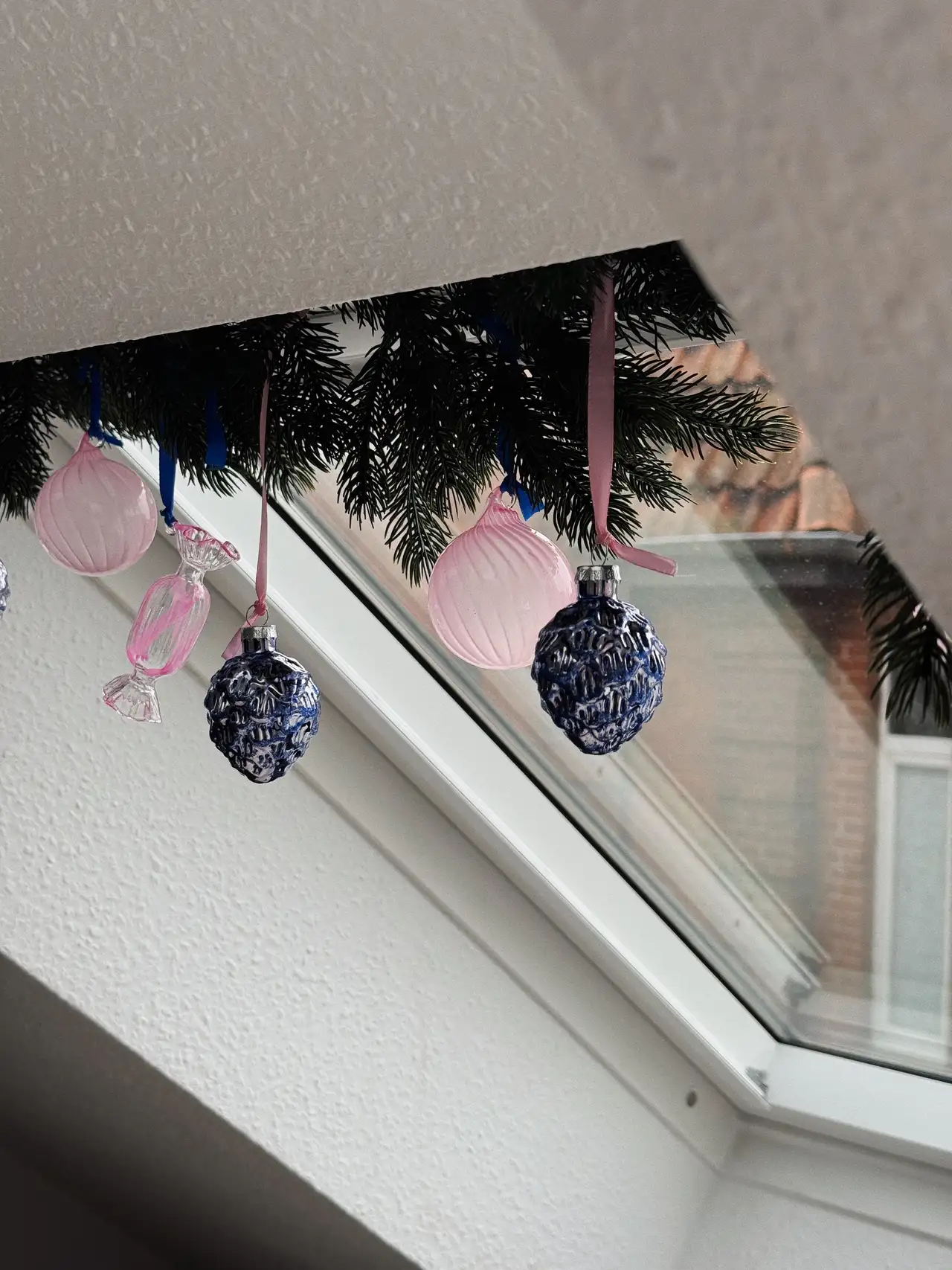 Una donna decora le finestre per tetti VELUX del suo soggiorno con ghirlande e decorazioni pendenti natalizie