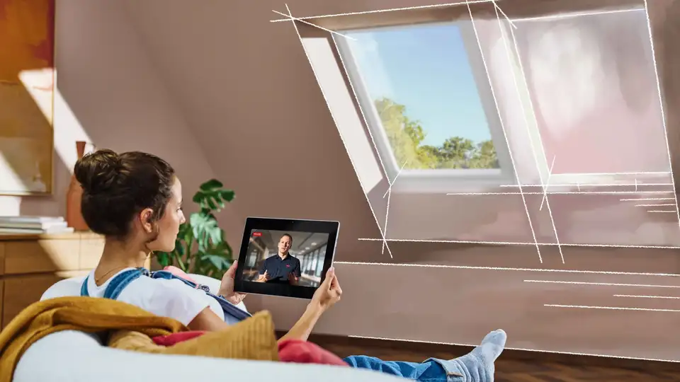 Dachzimmer mit schräger Decke, VELUX Dachfenster und einer Person, die auf ein Tablet schaut.