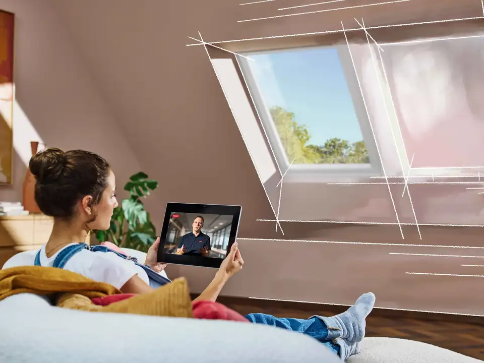 Dachzimmer mit schräger Decke, VELUX Dachfenster und einer Person, die auf ein Tablet schaut.