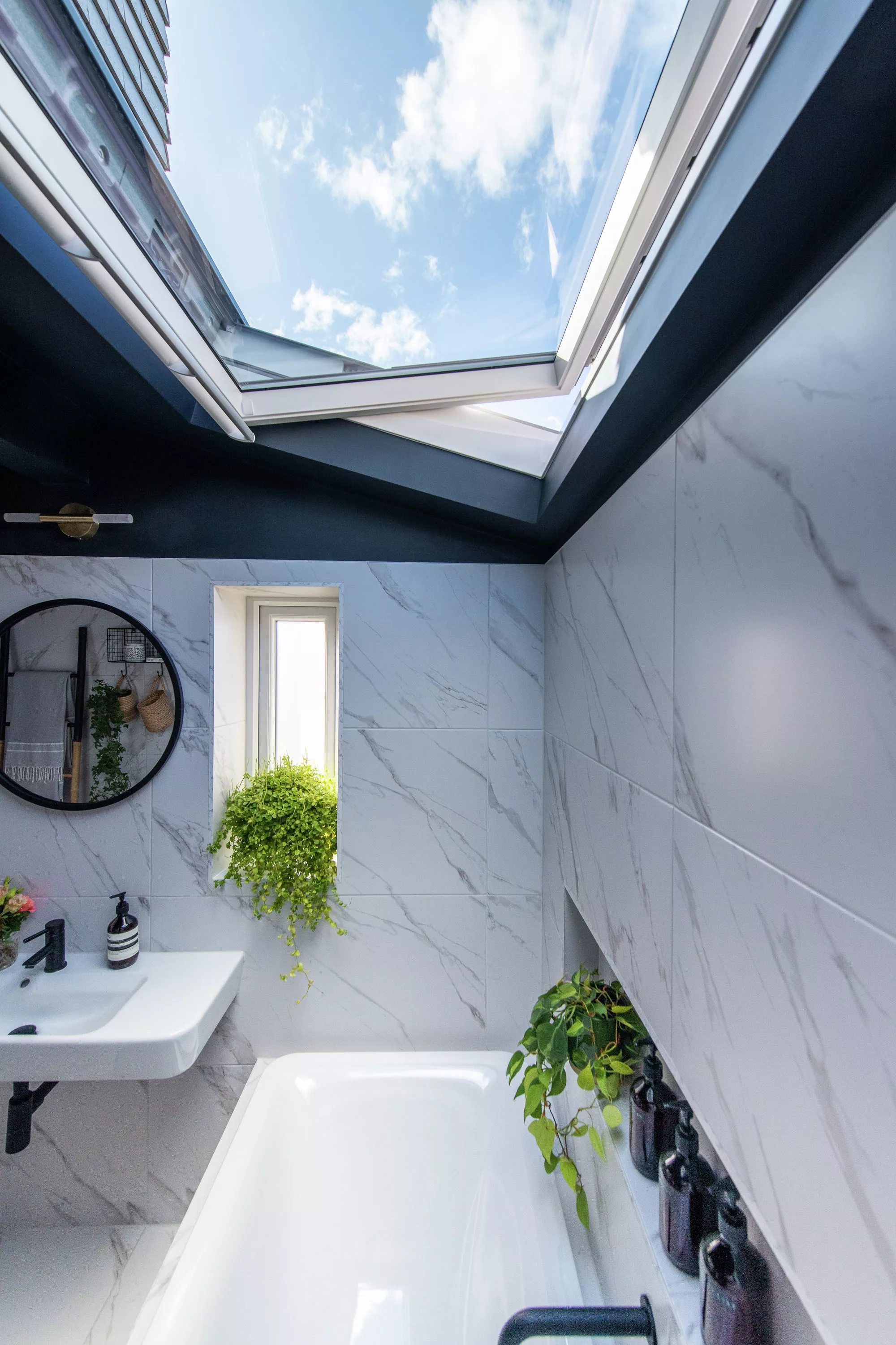 Luxurious marble bathroom with natural light from a VELUX skylight and green plants.