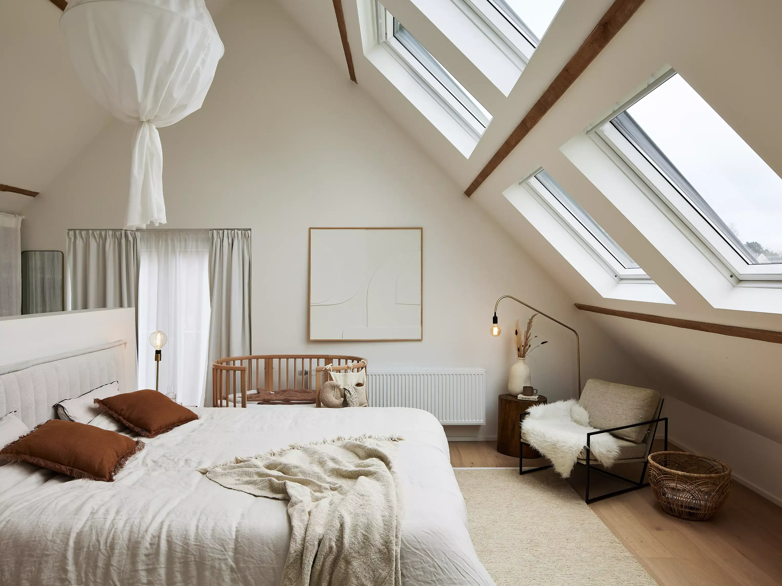 Chambre mansardée décorée dans un style apaisant et naturel, illustrant les principes d’une décoration de chambre réussie. Les fenêtres de toit apportent une lumière douce, tandis que les tons neutres, les textiles en lin, les poutres apparentes et le mobilier minimaliste créent une atmosphère chaleureuse et harmonieuse, parfaite pour un espace reposant.