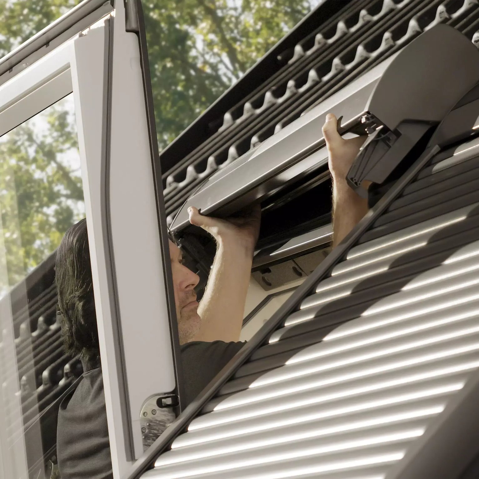 Man adjusting an open VELUX roof window on a metal roof.