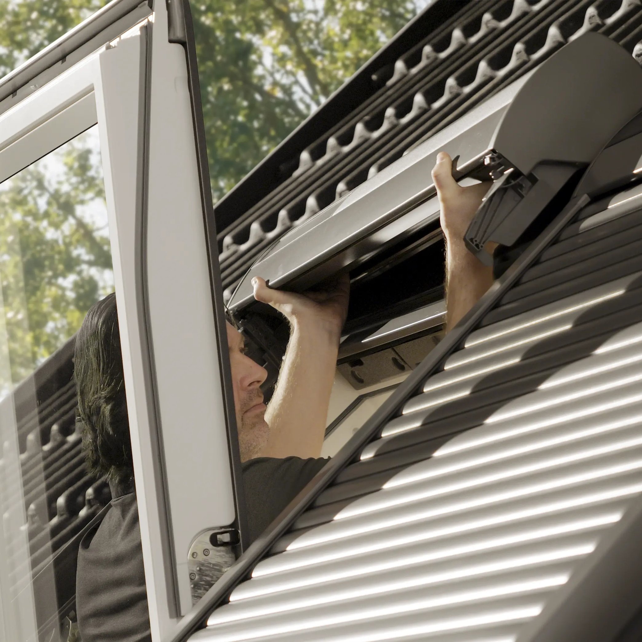 Man adjusting an open VELUX roof window on a metal roof.